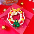Detailed view of handmade crochet Christmas wreath with miniature tree on red gift box - Green Christmas Tree Bib