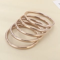 Macro shot of 18k rose gold plated titanium steel bangles stacked on a beige surface - Rose Gold 5-Piece Set