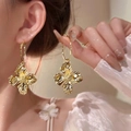 Elegant gold-tone 3D floral earrings with metallic pleated texture on a female model - Gold 3D Pleated Large Flower Earrings