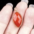 Handheld view of a marquise cut orange carnelian gemstone pendant with gold metal rim - Red Jasper