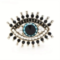 Golden Evil Eye brooch with black center gem and blue crystal accents on white background - Evil Eye Series 3