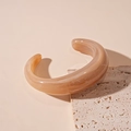 Detailed texture of a cream acrylic bangle with white marble patterns on a stone - Marbled Coffee Open Bangle