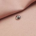 Makro-Detail einer flachen Edelstahl-Abstandshülse auf rosa Stoff für DIY-Schmuck - 3mm (100 Stück/Packung) / Stahlfarben