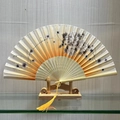Traditional Chinese folding fan with ink floral pattern and yellow tassel on stand - Radiant Clouds (Yellow)