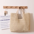 Bolso tote minimalista de paja beige con asas de cuero claro colgado en un gancho - Beige