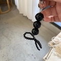Détail d'un porte-clés noir perlé avec fermoir argenté et nœud en résine brillante - Perles noires
