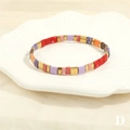 Detail of colorful Tila bead bracelet with golden spacers on a white shell plate - Red Purple Pink Orange Blue Gold