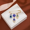 Detail of gold hamsa hand and blue evil eye charms on a tassel brooch pin - Hollow Hamsa Style (Z106-3)