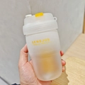 Close-up of hand holding a frosted transparent plastic tea cup with yellow SENDJUS logo - 580ml / White