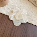 Detail shot of a cream-colored floral acetate hair clip with marble texture and engraved logo - Camellia Style / White / Large