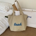 Beigefarbene Segeltuch-Einkaufstasche mit blauem Beach-Schriftzug auf Sisalteppich - Khaki mit Beach-Print