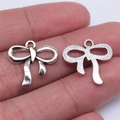 Silver bow-shaped metal pendants for DIY jewelry making shown on fingertips - Antique Silver