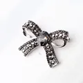 Bowtie brooch featuring dark grey crystals and silver metal base on white background - Black