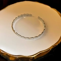 Brazalete geométrico plateado con bordes ondulados sobre bandeja de cerámica - Elipse / Plateado