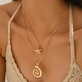 Golden layered necklace with starfish and spiral pendants worn by a female model - Gold Starfish Spiral