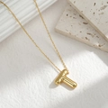 Detail of chubby golden letter T pendant on a necklace over a white textured stone base - Letter T