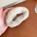 Detailansicht einer beige Pelz-Haarklammer, gehalten über einem hölzernen Tisch - Wolkenstil / Beige