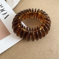 Detalle de la pulsera elástica de cuentas acrílicas ámbar sobre fondo revista Vogue - Estilo de Cuentas en Espiral / Pulsera-Ámbar