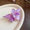 Macro shot of purple fabric hibiscus hair clip with realistic petals on a textured tray - Purple