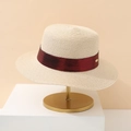 Detail of minimalist straw hat featuring a dark red ribbon and golden oval brand logo plate - Off White