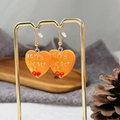 Boucles d'oreilles cœur de Noël en résine orange avec lettrage et nœud rouge - Cœur de Noël