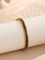 Detailaufnahme von geflochtenem Goldarmband mit schwarzen Zirkonia-Steinen auf Stein - Goldfarben Schwarze Zirkonia