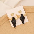 Detailed close-up of Bohemian bull skull earrings with gold heart studs on display card - Black