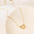 Minimalistische Herz-Halskette aus Gold-Titanstahl auf einem Keramikteller - Goldenes Hohles Herz