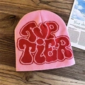 Detail of pink knitted beanie with red Top Tier jacquard lettering on wooden background - Pink