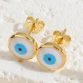 Close-up of golden evil eye stud earrings with blue enamel on a white stone surface - Round Stud Earrings
