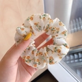 Witte kanten scrunchie met gele bloemmotieven en lange linten vastgehouden in hand - #1 De Kleine Gele Bloem In Het Verhaal