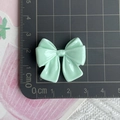 Macro detail of a 3.5cm light green resin bow charm next to a ruler for size scale - Green