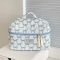 Quilted cosmetic bag with blue bow patterns, top handle, and elegant zipper tassel detail - Makeup Bag / Blue