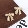 Elegantes pendientes de lazo dorado con perlas blancas sobre fondo de madera rústica - Stud aretes