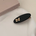 Detail of a chic black oval hair clip with a golden bow on a white decorative base - Black