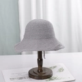 Light grey knitted bucket hat with chin strap displayed on a wooden stand - M (56-58cm) / Gray