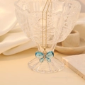 Detail van een blauwe kristallen vlinderhanger aan een gouden ketting op zijde - Meer blauw