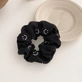 Close-up of black fabric scrunchie with white smiley face patterns on a ceramic plate - Bubble Cotton Smiley Face / Black