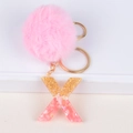 Detail of pink faux fur pompom and resin letter X keychain with gold flakes on white stand - Letter X