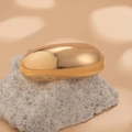 Close-up of a polished gold oval hair accessory on a minimalist stone display - Gold 1090573