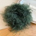 Detailed view of forest green curly plush scrunchie on a warm wooden tabletop - Green