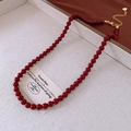 Detail of red beaded necklace with golden lobster clasp and heart charm on beige tray - Red