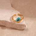 Close-up of golden wavy band ring with a pear-shaped light blue gemstone on stone base - Gold Waterdrop