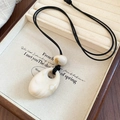 Détail du pendentif goutte crème sur collier cordon noir posé sur plateau en bois - Blanc