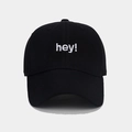 Dettaglio ravvicinato del ricamo bianco 'hey!' su un cappellino da baseball nero - Regolabile / Nero