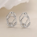 Orecchini geometrici cavi irregolari con zirconi in finitura argento su sfondo beige - Argento