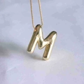 Macro shot of 3D balloon style letter M pendant with starburst texture on gold chain - M