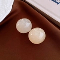 Detail view of round cream resin earrings with marble texture on elegant silk background - White
