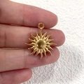 Macro shot of a golden sun-shaped stainless steel pendant held between fingers - 7 Slender Rays Sun
