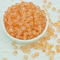 Detailed macro view of frosted orange-pink glass beads with gold foil in a ceramic bowl - 6mm Orange with Gold Glitter